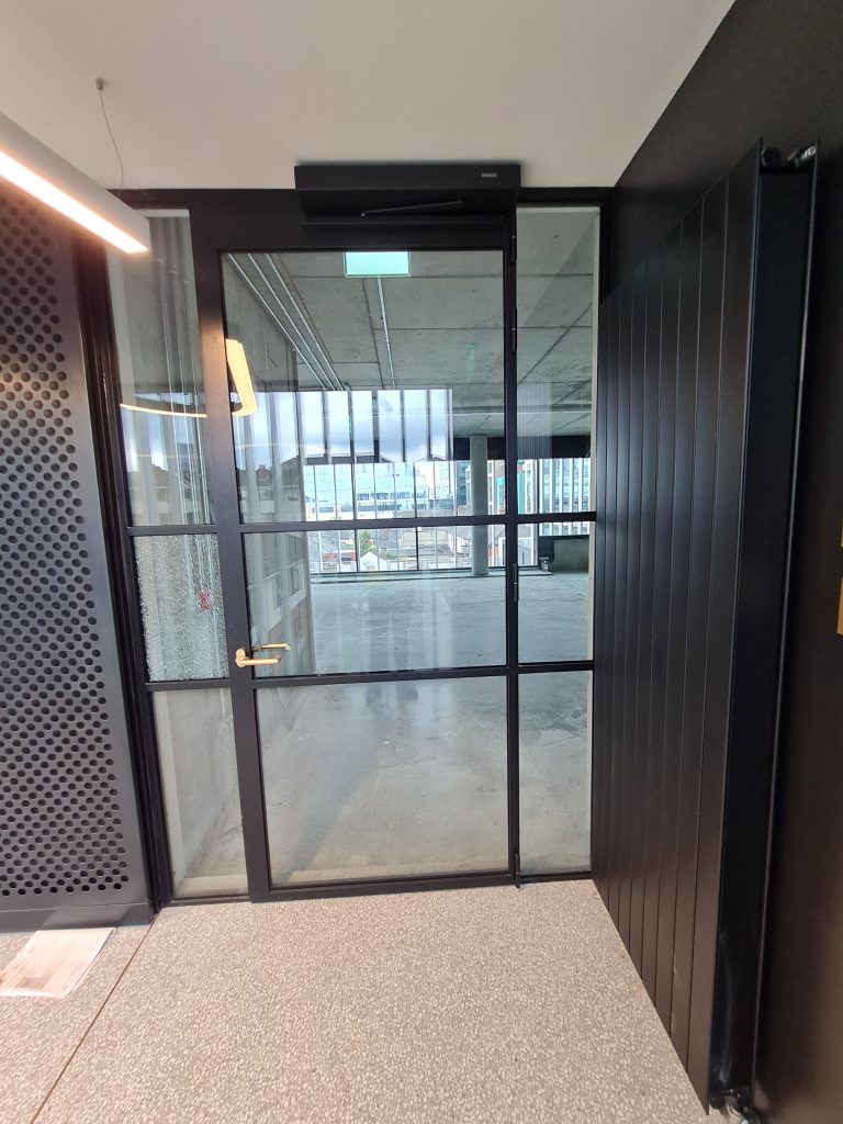Closed black steel framed glass door with matching black door closer beside black walls