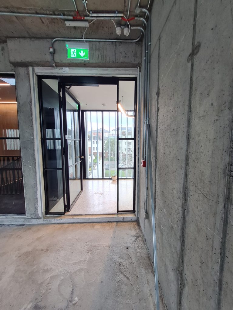Open Single glass door with black steel frame and adjacent steel frame screen exiting to lift lobby