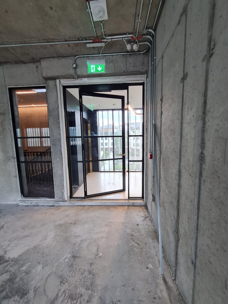 Open Single glass door with black steel frame and adjacent steel frame screen in commercial building
