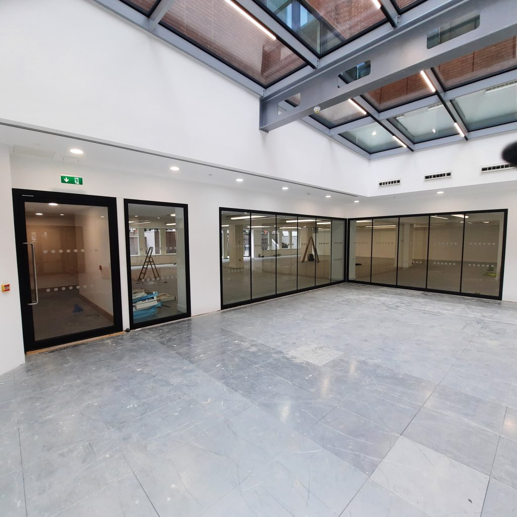 large open plan communal space in modern commercial building with glazed screen walls and glazed atrium ceiling