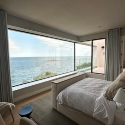 View from inside a modern interior-designed bedroom with a 2.5 metre high, 5 metre long corner window overlooking the sea.