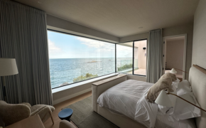 View from inside a modern interior-designed bedroom with a 2.5 metre high, 5 metre long corner window overlooking the sea.