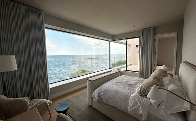 View from inside a modern interior-designed bedroom with a 2.5 metre high, 5 metre long corner window overlooking the sea.