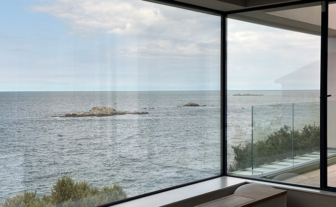View of irish coast and sea through a 2.5 metre high corner window. To the right, there appears to be a small covered balcony area.