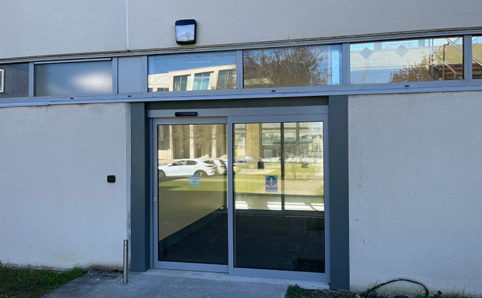 An angled view of a sliding automatic door with a glass screen. The door slides over the screen to open and allow people to enter or exit.