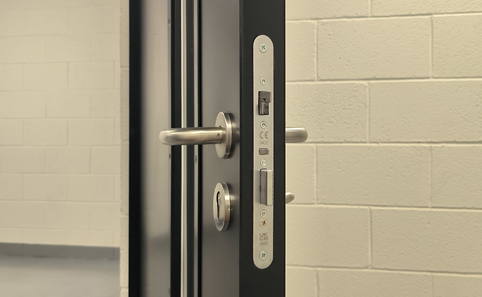 A view of a return to door lever, lockcase, escutcheon and thumbturn on a black steel door in a basement area